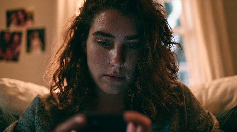 Девушка ночью смотрит в смартфон — привычка следить за бывшим в соцсетях