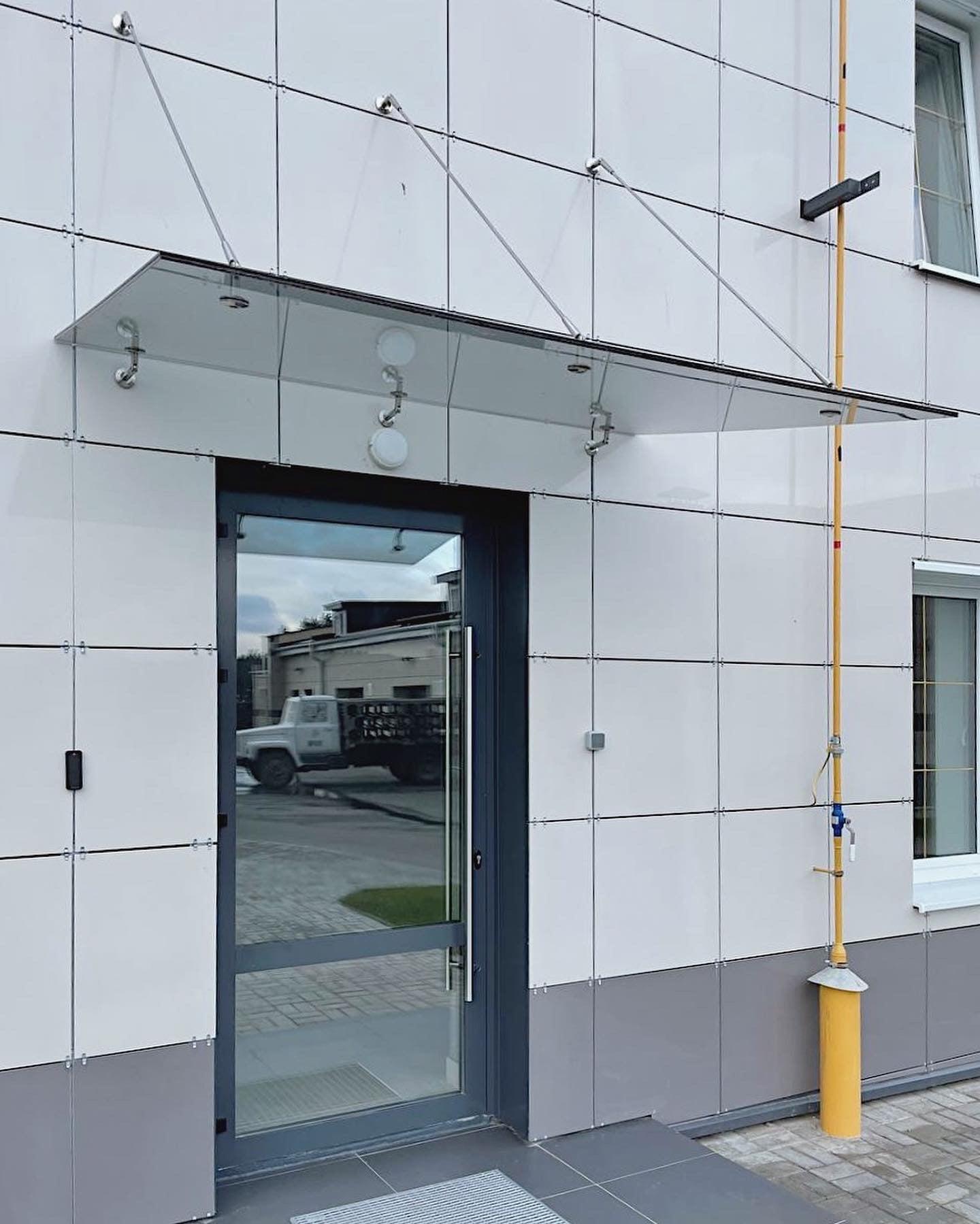 стеклянный козырек на вантах из нержавеющей стали над входом в современное здание, крепеж на фасадные стойки