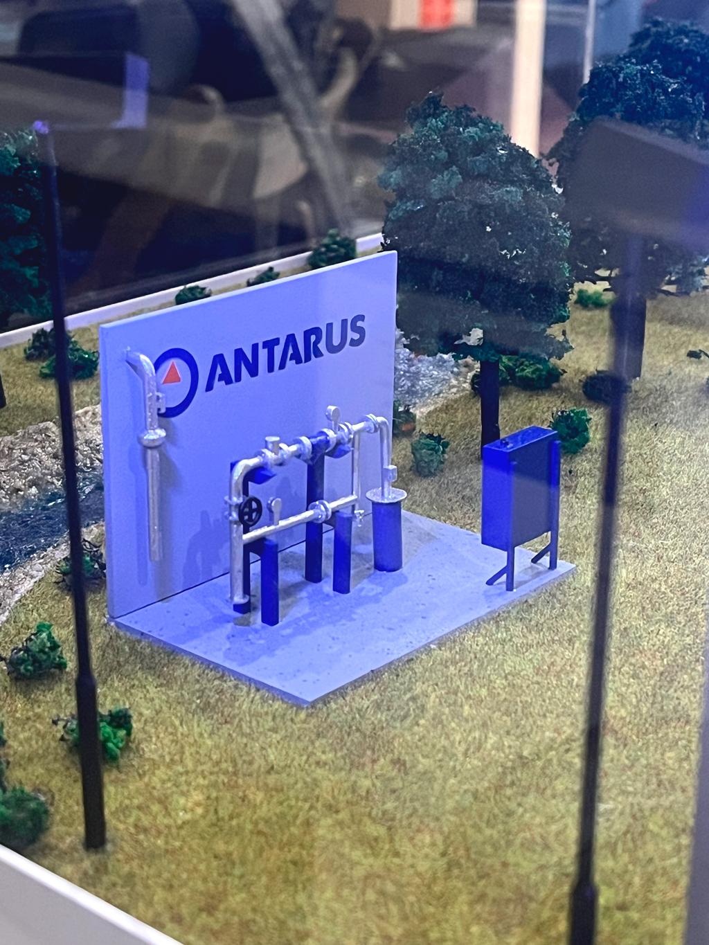 Миниатюрная модель насосной станции, предназначенной для перекачки воды или других жидкостей.   На Масштабном макете демонстрируется несколько вертикальных насосов с электродвигателями (синие детали). • Трубопроводы, соединяющие насосы и выходную магистраль. • Щит или емкость рядом — скорее всего, элемент водоснабжения (гидроаккумулятор, фильтр или электрооборудование). • Логотип и название компании (Antarus) — это может быть производитель насосного оборудования.  Назначение: Такие насосные станции используют: • Для подачи воды в системы водоснабжения (населенных пунктов, промышленных объектов). • Для повышения давления в системе. • В сельском хозяйстве (орошение). • Для противопожарного водоснабжения.