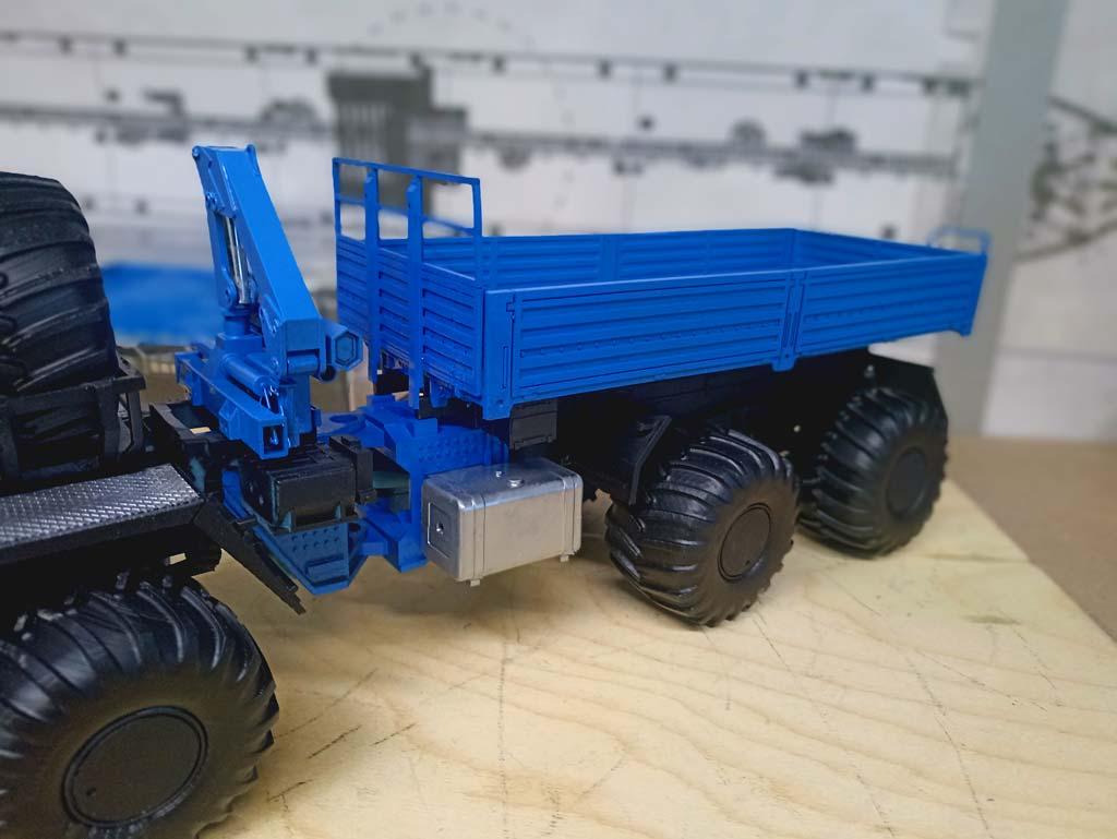 Детализированная масштабная модель грузового автомобиля КАМАЗ с прицепом (масштаб 1:43). Кабина выполнена в насыщенном синем цвете с контрастными чёрными элементами, дополнена красными рейлингами на крыше и боковыми лестницами. Массивные чёрные колёса с выраженным протектором подчёркивают внедорожный характер модели. Прицеп также окрашен в синий цвет, оснащён бортами и реалистичными крепёжными элементами. Модель демонстрирует ключевые детали: решётку радиатора с логотипом КАМАЗ, боковые зеркала, дверные ручки, элементы ходовой части. Идеально подходит для коллекционирования, оформления выставок, посвящённых грузовой технике, или использования в презентационных материалах производителей автотранспорта.