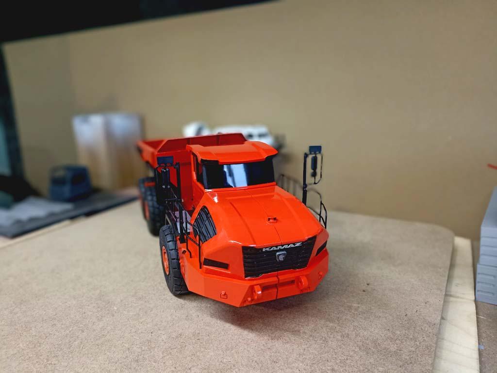 Детально проработанная масштабная модель карьерного самосвала КАМАЗ-6561 «Геркулес» грузоподъёмностью 40 тонн. Модель выполнена в насыщенном оранжевом цвете, подчёркивающем индустриальный характер техники. отчётливо видны элементы шарнирно-сочленённой рамы, массивные колёса размером 29,5 R25, кабина с боковыми зеркалами и самосвальная платформа. Проработаны детали передней решётки с логотипом «КАМАЗ», защитные поручни и элементы ходовой части. Модель демонстрирует особенности конструкции последовательного гибрида: сочетание дизельного двигателя (500 л. с.) и электродвигателя (525 кВт). Подходит для коллекционирования, оформления тематических выставок, посвящённых строительной и карьерной технике, а также для использования в презентационных материалах производителей спецтехники.