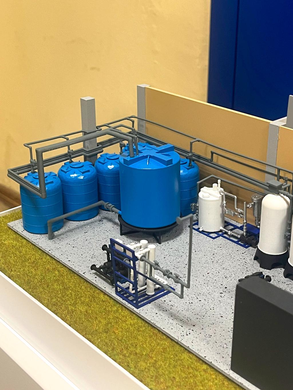 Масштабный макет изготовленный в нашей макетной мастерской подобные станции применяются на производствах, в котельных, в жилых комплексах и других объектах, где требуется предварительная фильтрация и подготовка воды для технических или бытовых нужд.  Синие ёмкости (резервуары) — это, баки для хранения воды (очищенной или исходной), а также ёмкости для хранения реагентов. • Цилиндрические белые и серые сосуды — это фильтры или фильтрующие колонны (например, механический фильтр, фильтр с ионообменной смолой или активированным углём). • Трубопроводы и арматура — соединяют всё оборудование и отвечают за подачу, распределение и отвод воды на различных стадиях очистки. • Платформы и шкафы — здесь может находиться электроника, насосы, датчики и запорная арматура для автоматизации процессов.