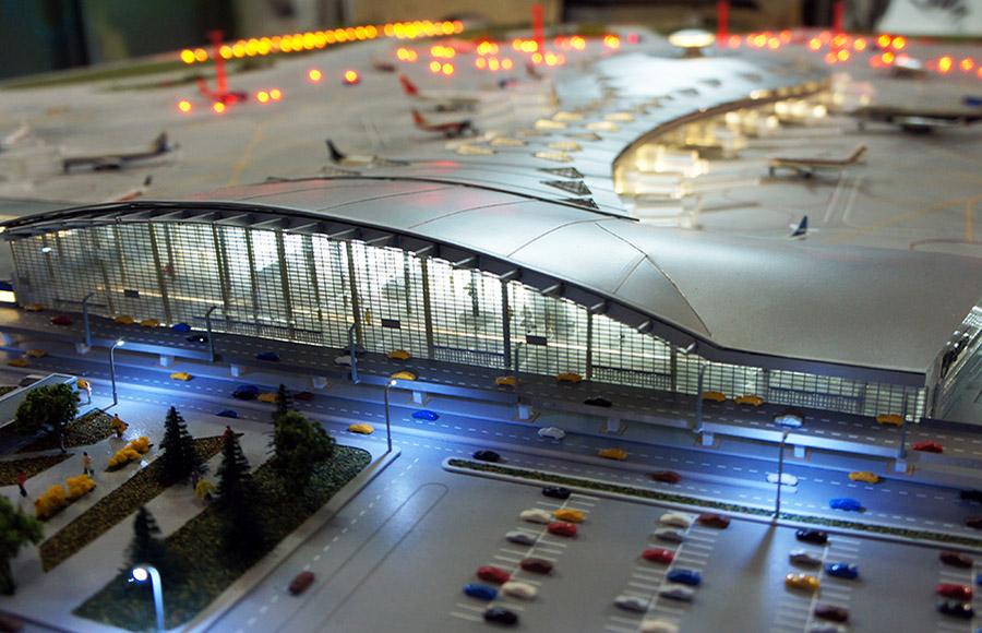 Макет терминала аэропорта, который включает в себя здание терминала, взлетно-посадочные полосы, рулежные дорожки и прилегающую инфраструктуру. Это трехмерная модель, созданная для визуализации архитектурного проекта и демонстрации потенциальным покупателям или инвесторам. Макет позволяет увидеть, как будет выглядеть будущее строительство, включая расположение зданий, инфраструктуру и ландшафтный дизайн.