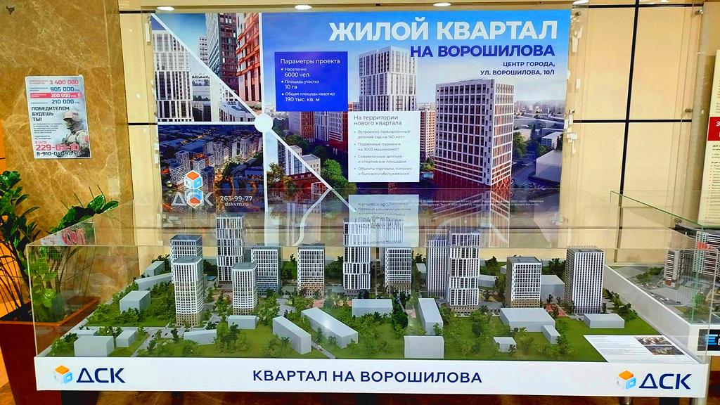 На фотографии изображен архитектурно-инженерный макет аэропортового комплекса с элементами аэродромной инфраструктуры. Это масштабная модель аэровокзального комплекса и прилегающей территории перрона аэропорта. На макете детально показаны:  • Сам пассажирский терминал (аэровокзальное здание); • Краткосрочная автодорога и подъездные пути с парковкой перед терминалом; • Перрон аэропорта с моделями пассажирских самолетов, расположенных у телетрапов; • Осветительные системы (имитация огней ВПП и рулежных дорожек); • Дополнительные элементы инфраструктуры (сигнальные огни, диспетчерские вышки и т.д.).  Макет необходим для наглядной демонстрации архитектурных и инженерных решений, оценки взаимного расположения объектов, а также для планирования пассажиропотока и наземного транспорта. 2. Защита проекта и презентация:   Используется для презентаций перед инвесторами, государственными органами, заказчиками, а также при проведении публичных слушаний. 3. Обучение и моделирование процессов:   Может применяться для обучения сотрудников аэропорта, отработки логистики обслуживания воздушных судов и пассажиров. 4. Маркетинг и реклама:   Дает возможность визуализировать проект для потенциальных арендаторов, подрядчиков или клиентов.  Такой макет — важный инструмент в современных строительных и инфраструктурных проектах, позволяющий принимать более обоснованные решения на этапах проектирования и реализации.