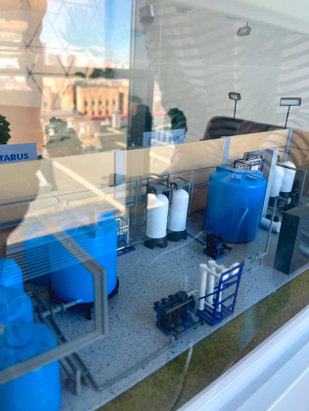 Макет технологического процесса обработки воды или химических веществ. В модели видны резервуары, трубопроводы и оборудование для фильтрации и хранения. Этот объект может быть частью системы водоснабжения или переработки, предназначенной для очистки и подготовки воды к дальнейшему использованию. Макет водоподготовки и очистки водопроводной воды, накрыт прозрачным колпаком. Изготовлен макетной студией на заказ для демонстрации на выставке в Москве.