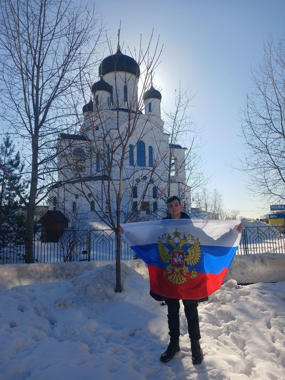 Артём Алексеевич с флагом Российской Федерации на фоне православной церкви. 