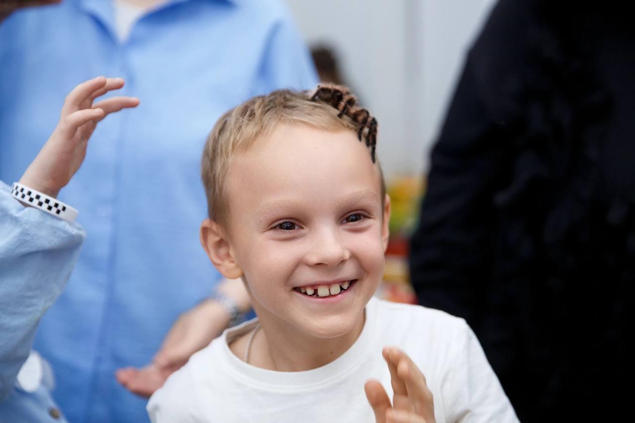 ребёнок улыбается с безопасным пауком на голове во время шоу AMStudio