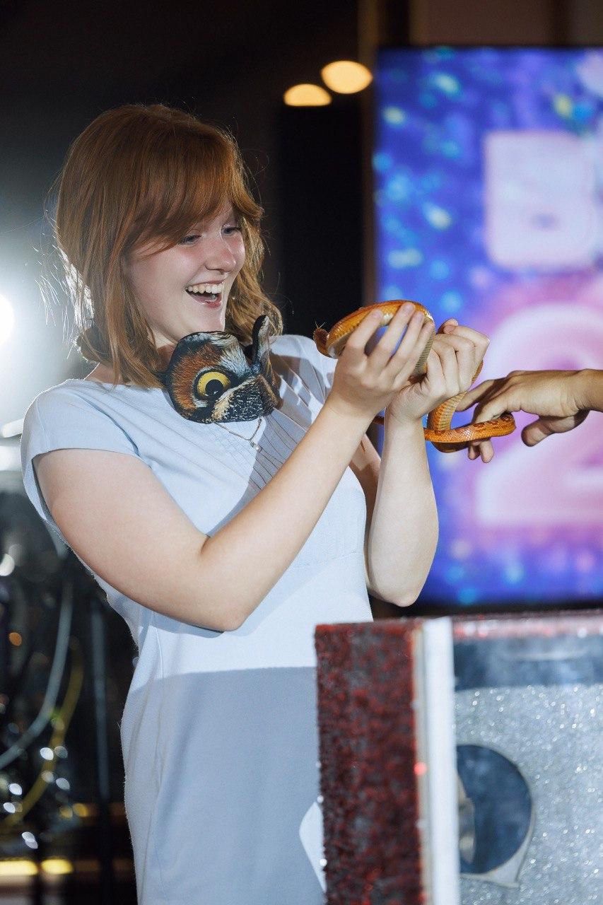 Шоу с животными AMStudio в Москве — гостья с улыбкой держит в руках змею во время программы Треш-коробка